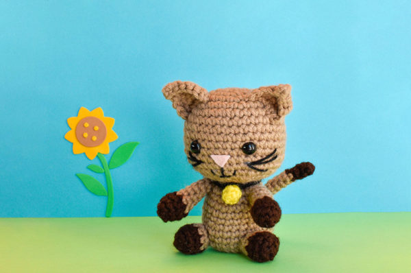 a crochet kitten doll against a blue and green backdrop