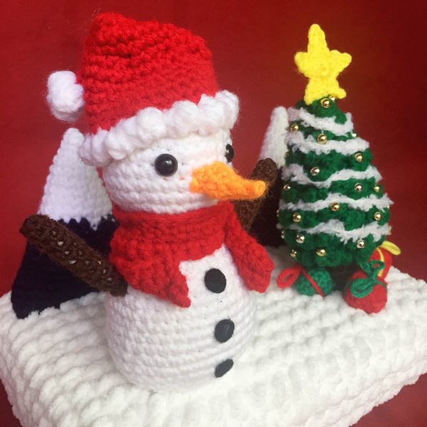 diorama of a crochet snowman with a crochet christmas tree and crochet mountains