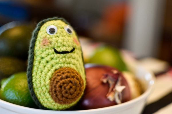 a crochet avocado sitting in a bowl with some real fruits and vegetables