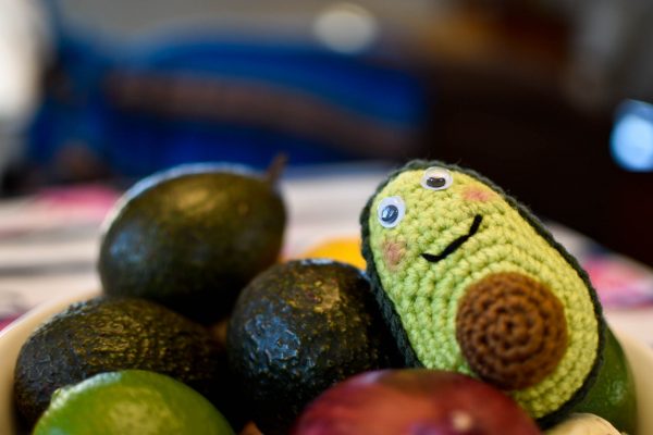 a crochet avocado sitting in a bowl with some real fruits and vegetables