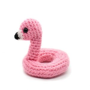 side view of a small crochet flamingo floatie toy against a white background
