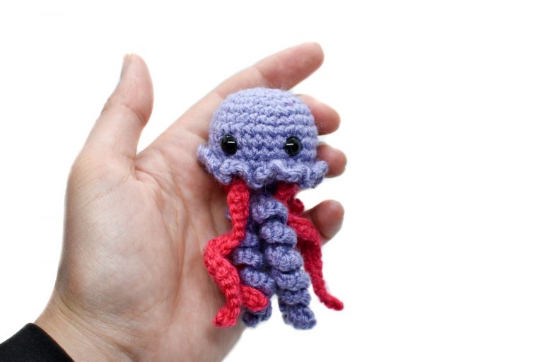 a small crochet purple and pink jellyfish toy held up against a white background