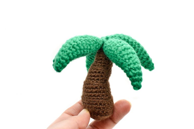 a small crochet palm tree toy held up against a white background