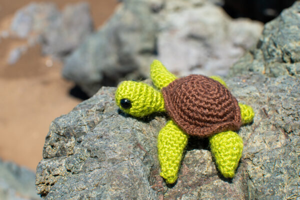 a small crochet sea turtle toy sitting on a rock at the beach