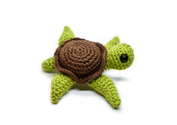 side view of a small crochet sea turtle toy with a white background