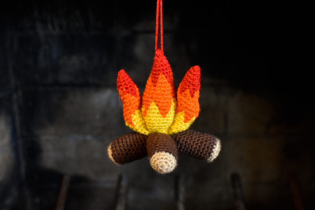 a small plush crochet campfire hanging against a brick fireplace