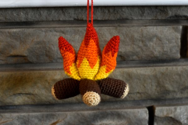 a small plush crochet campfire hanging against a brick fireplace