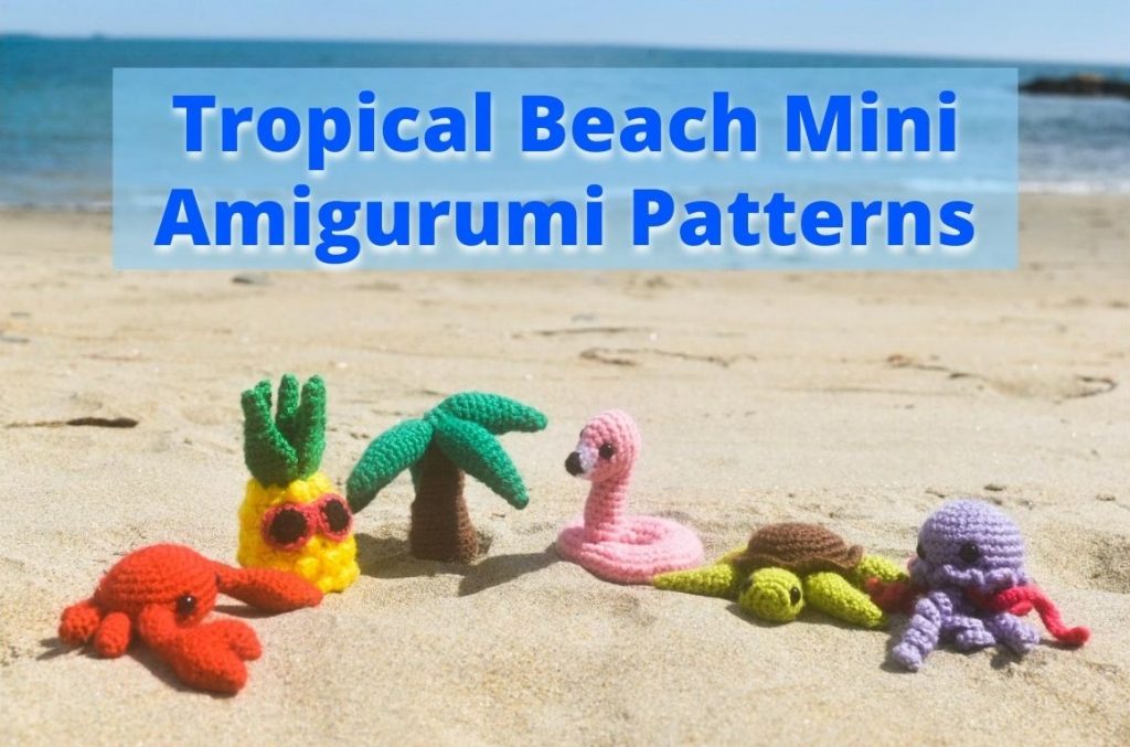 small crochet dolls of a crab, a pineapple, a palm tree, a flamingo floatie, a sea turtle, and a jellyfish sitting on a beach