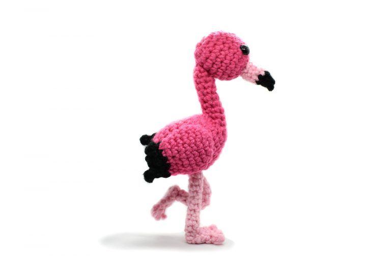 a crochet pink flamingo standing on one leg