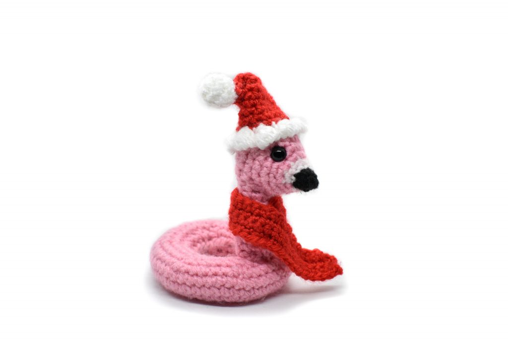 a small crochet flamingo floatie wearing a Santa hat and red scarf