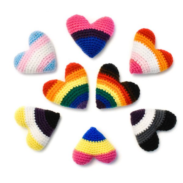 8 crochet hearts with pride colours. In the middle are two hearts in the rainbow Pride & Inclusive Pride flag colours, and around them are hearts depicting the Trans, Bisexual, Lesbian, Asexual, Pansexual, and Non-Binary flag colours.