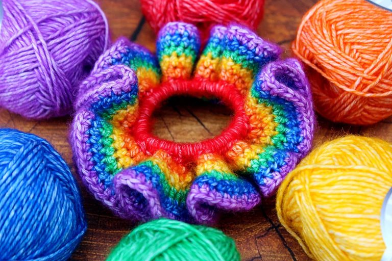 a rainbow coloured crochet hair scrunchie sitting on a table surrounded by yarn