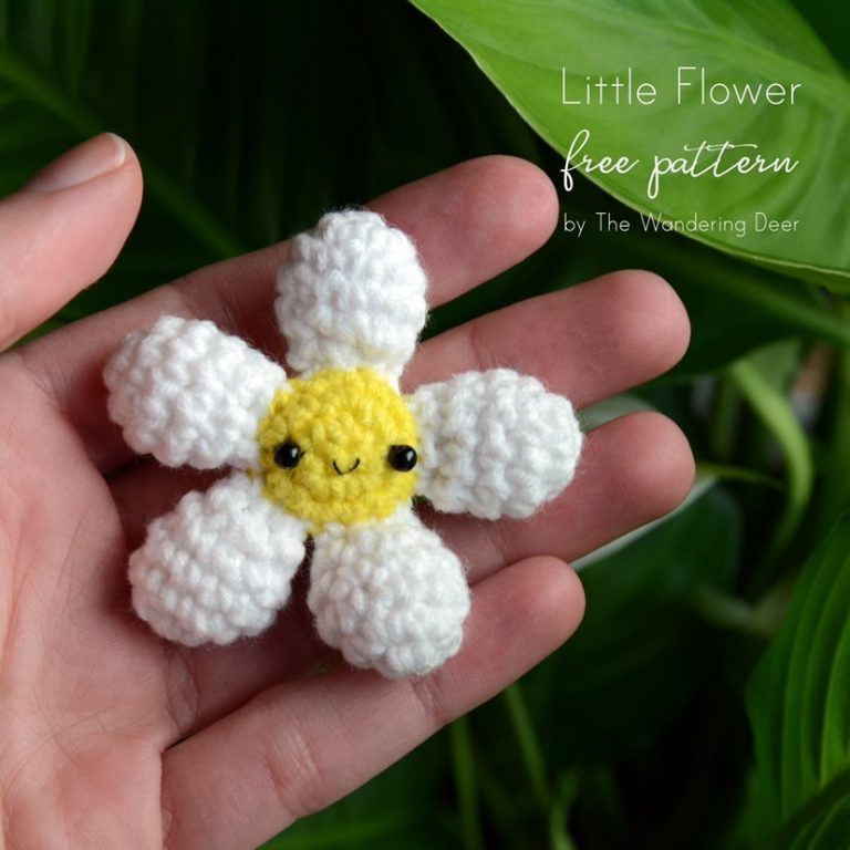 a small crochet daisy with a yellow middle and white petals. There is a happy face in the middle.