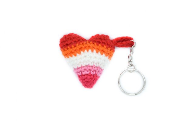 a small crochet heart keychain in the lesbian flag colours against a white background. From top to bottom: red, orange, white, light pink, dark pink