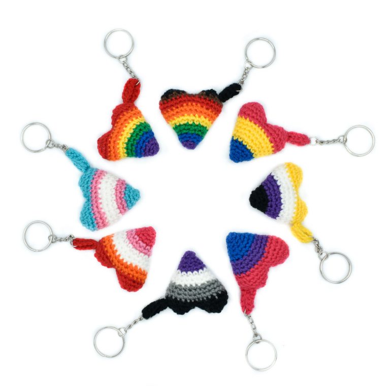 8 small crochet heart keychains with pride colours, arranged in a circle. The pride flags are: Rainbow, Inclusive Rainbow, Trans, Bisexual, Lesbian, Asexual, Pansexual, and Non-Binary flag colours.