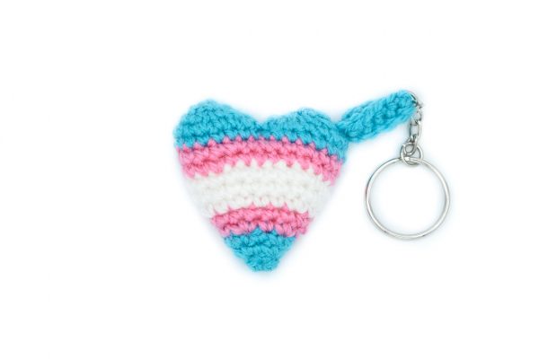a small crochet heart keychain in the trans flag colours against a white background. From top to bottom, the colours are: light blue, pink, white, pink, light blue