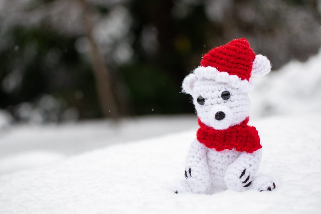 a stuffed crochet polar bear wearing a Santa hat and a red scarf, sitting in the snow.