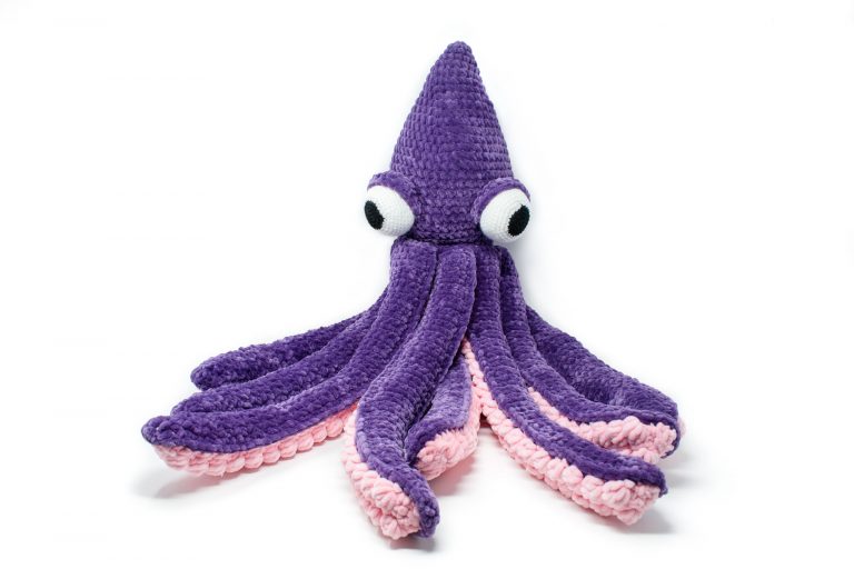 a large crochet kraken made out of chunky yarn. The body is purple and the underside of the tentacles are light pink.