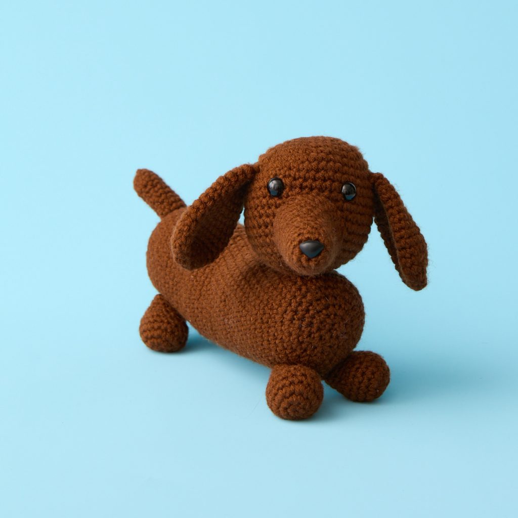 a cute stuffed crochet brown dachshund dog on a blue background