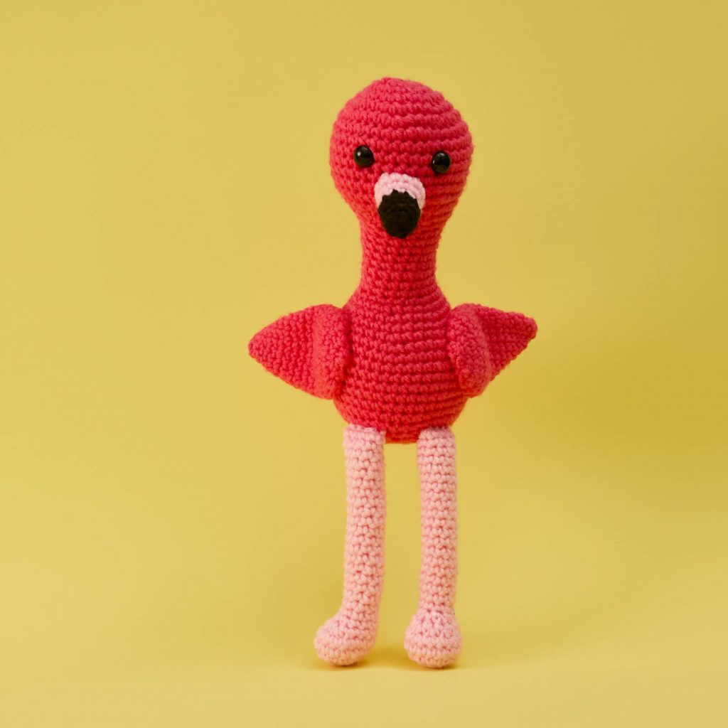 a cute stuffed crochet flamingo on a yellow background