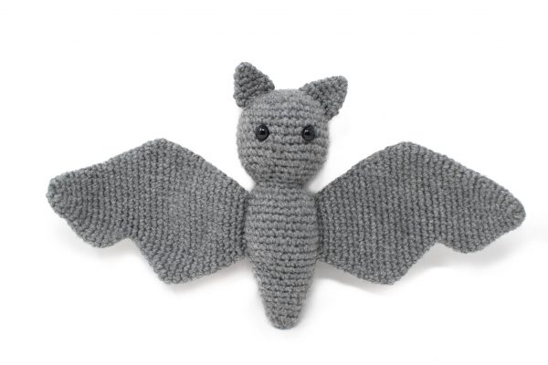 a stuffed crochet grey bat lying on top of a white background
