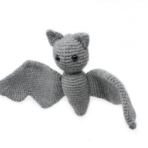 a stuffed crochet grey bat shown hanging in front of a white background