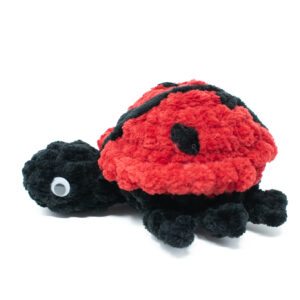 a crochet ladybug toy made from soft chunky chenille yarn, on a white background
